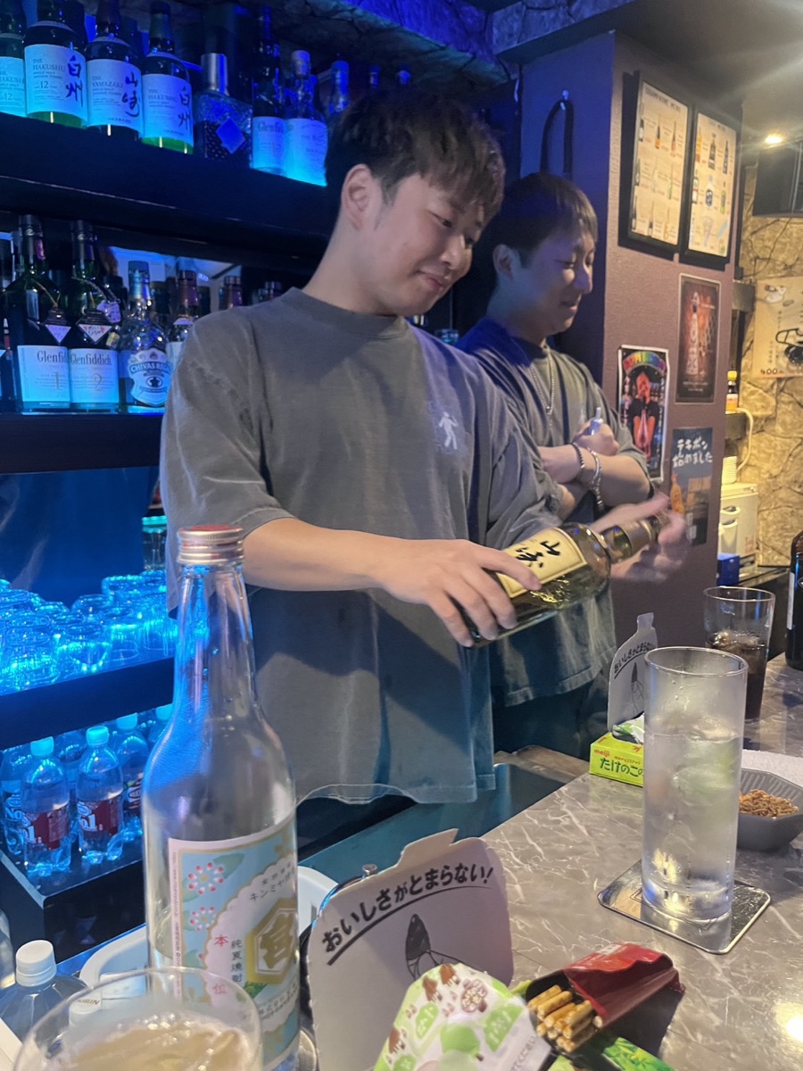 BAR NOMENOMEのカウンター。ボトル棚の前でドリンクを作る店主ミッチーとショータ